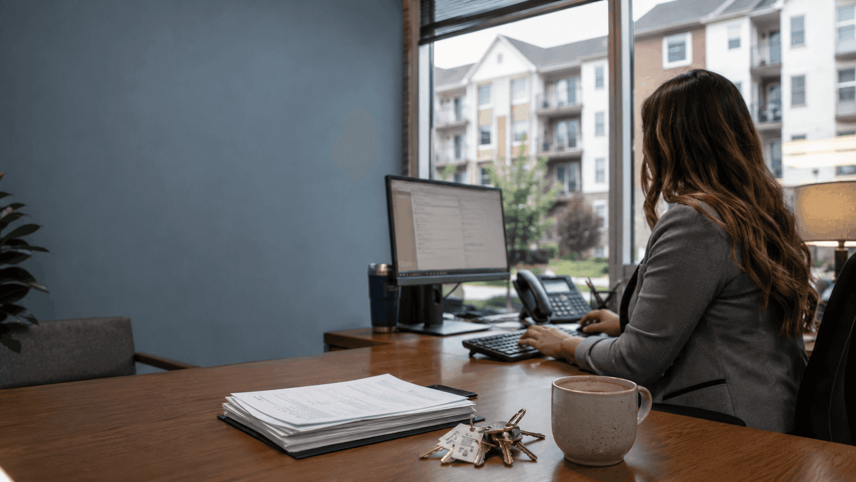 Property manager working at a leasing office desk with lease paperwork and apartment keys, illustrating IT support for property management companies