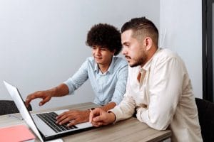 Two young men working together on a laptop in a modern office setting.